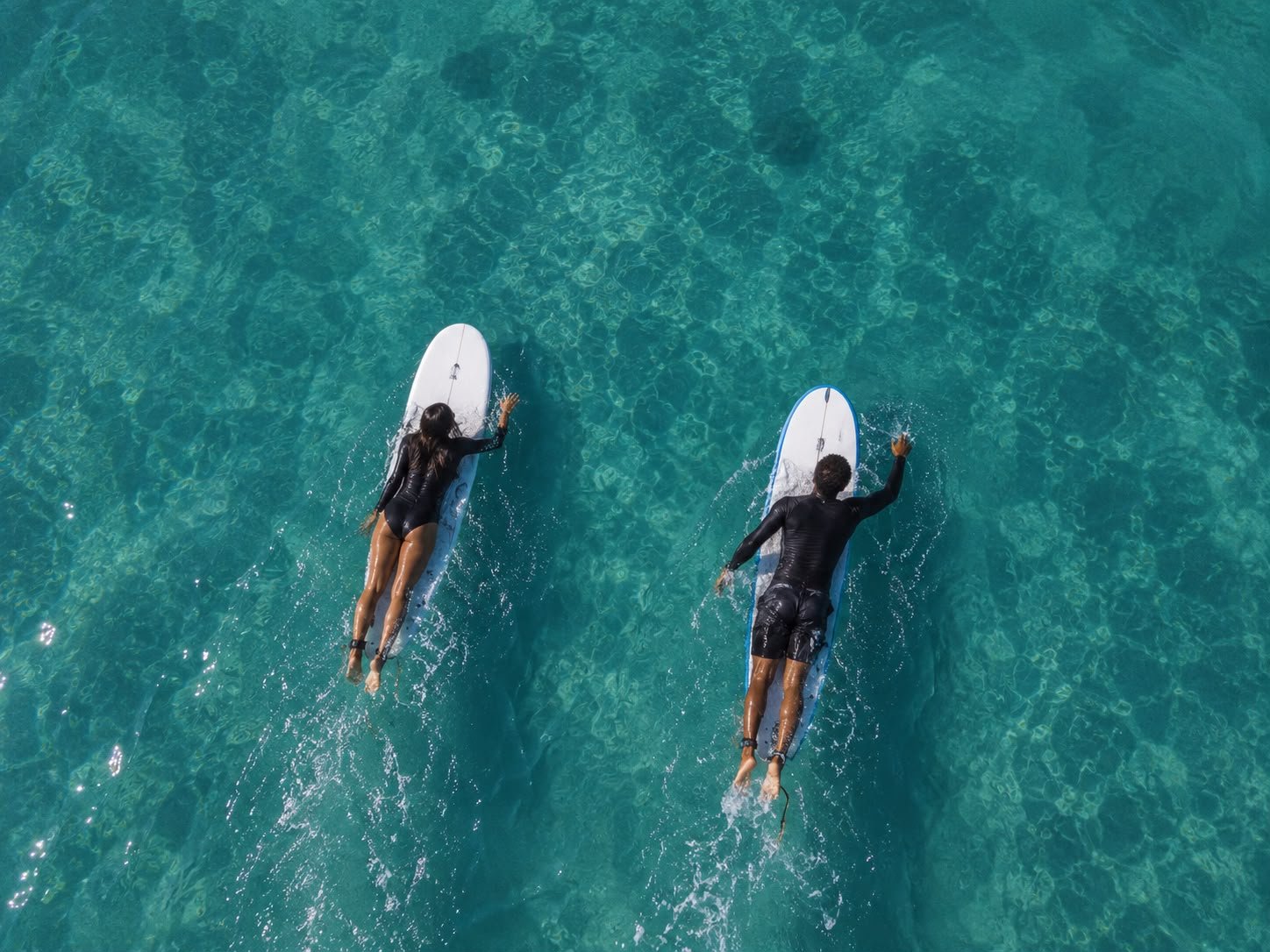 Due surfisti remano nell'acqua cristallina visti dall'alto
